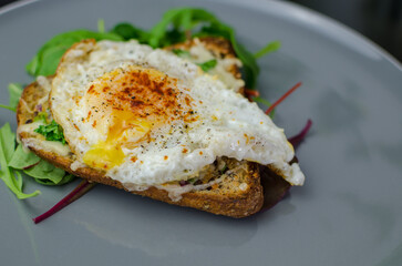 Fried egg on a bread roll with greens on a grey plate