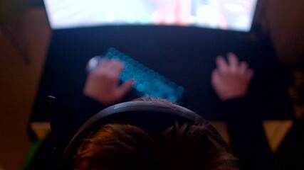 A dedicated gamer intensely focused on a bright screen while using a keyboard and a headset