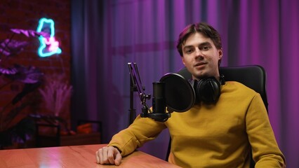 Man host in headphones sitting at table and recording interview video in loft podcast studio using...