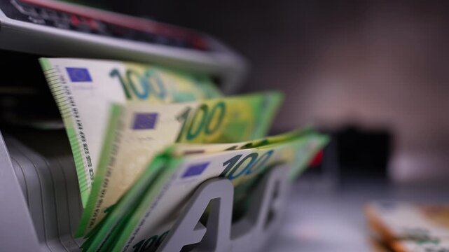New green banknotes of one hundred euro appear from cash counting machine. Bank equipment working. Close up. Blurred backdrop.