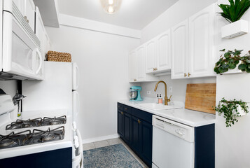 A kitchen with white and blue cabinets, white countertop, and gold faucet.