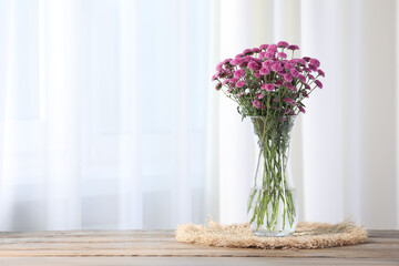 Beautiful pink flowers in vase on wooden table indoors. Space for text