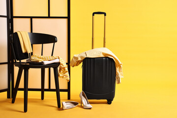 Suitcase with messy clothes and chair on yellow background