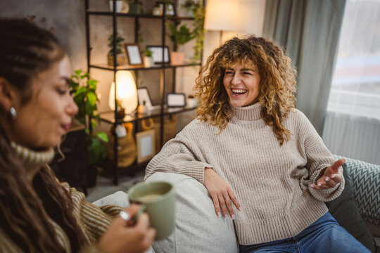 two young adult female friends sit on sofa and enjoy while chatting