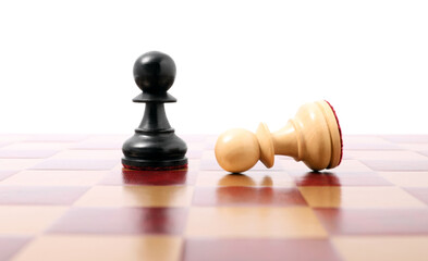Pawn near fallen black one on wooden checkerboard against white background. Competition concept