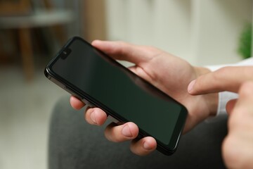 Man using smartphone with blank screen indoors, closeup