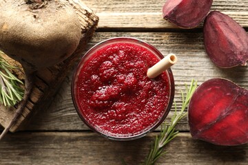 Fresh beetroot smoothie in glass, rosemary and cut vegetable on wooden table, flat lay