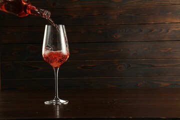 Pouring rose wine into glass at wooden table, space for text