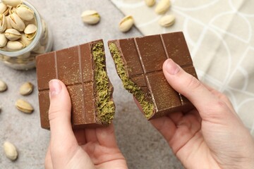 Woman breaking Dubai chocolate bar with pistachios and knafeh at grey table, closeup