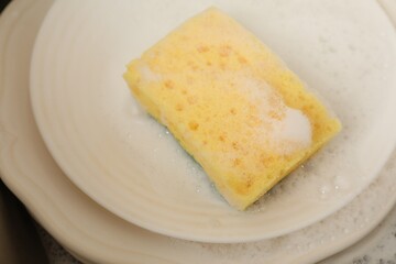 Yellow sponge, dishes and foam in sink, closeup