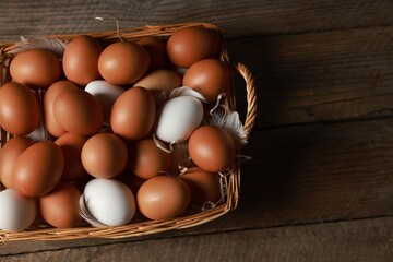 Many raw eggs in basket on wooden table, above view