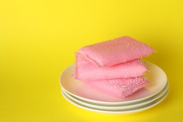 Stack of sponges and plates on yellow background, closeup. Space for text