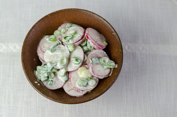 Fresh summer salad - radish and spring onions with sour cream - in a brown rustic bowl, top view
