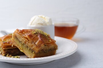 Delicious baklava with crushed nuts and ice cream on grey table, closeup. Space for text