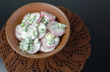 Fresh summer salad - radish and spring onions with sour cream - in a brown rustic bowl, top view
