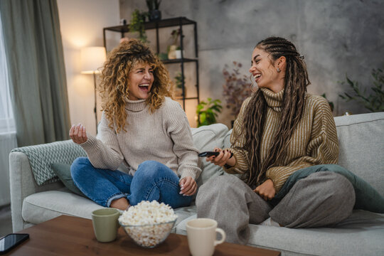 female friends laugh and relax watch TV on sofa at home