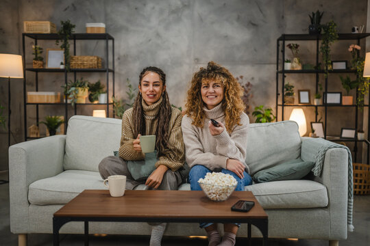 female friends laugh and relax watch TV on sofa at home