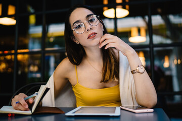 Pensive young lady working with notebook and gadgets at table in street cafe