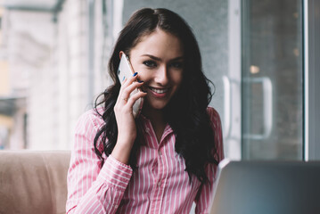 Obraz premium Smiling businesswoman talking on smartphone while working remotely in cafe
