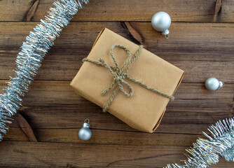 New Year's gift. A gift in craft paper, tinsel and Christmas balls on a wooden background.