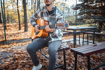 Guitarist, dressed in a cozy plaid shirt, strums an acoustic guitar while seated among autumn...