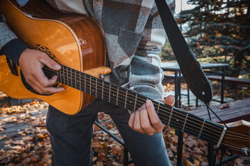 Guitarist, dressed in a cozy plaid shirt, strums an acoustic guitar while seated among autumn...