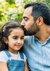 Fototapeta premium Father is kissing his daughter on the forehead while enjoying time together outdoors