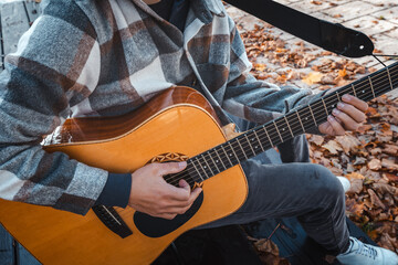 Guitarist, dressed in a cozy plaid shirt, strums an acoustic guitar while seated among autumn...