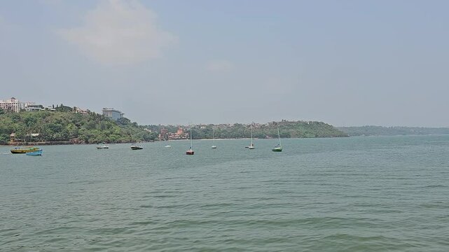 As seen form the Dona Paula viewpoint featuring small boats and a hilly green landscape in the background. The clear sky adds to the tranquil feel.
