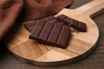 Pieces of delicious dark chocolate bar on wooden table, closeup