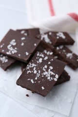 Pieces of chocolate with salt on white table, closeup