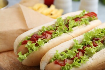 Tasty hot dogs with lettuce, ketchup and potato fries on table, closeup