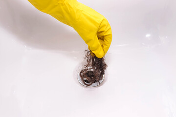 Bathroom drain clogged with hair clump and grime. Woman's hand in  yellow glove pulls hair out of...