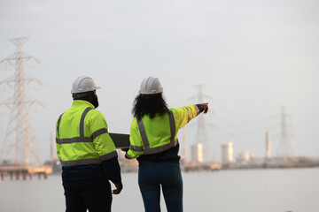 A man and a woman, both engineers, wear green safety jackets while working at a renewable energy...