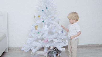 A boy decorates a Christmas tree in a white room.