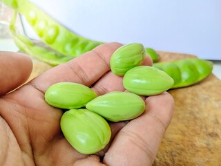 close up of some petai without skin on hand and wooden chopping board