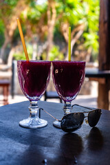 Delicious Prickly Pear Juice in a Clear Glass on Rustic Wooden Table for Healthy Refreshing Drink and Natural Wellness. Bananas in the Background. Sunglasses in Foreground
