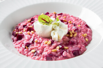 A plate of vibrant pink beetroot risotto topped with a poached egg, pine nuts, and fresh microgreens. The dish is elegantly presented in a white bowl, showcasing rich textures and colors.