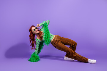 Trendy young woman in vibrant outfit posing dynamically on a purple background