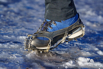 Foot of a man wearing black pants and blue mountain boots with crampons. Crampons, a type of spike,...