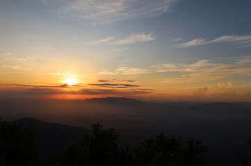 The picture depicts a sunrise on a countryside landscape with foggy mountains and clouds. 
