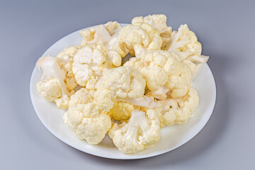 Pieces of raw cauliflower on dish on a gray background