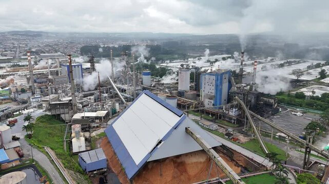 Vis&atilde;o a&eacute;rea de uma ind&uacute;stria brasileira de papel e celulose, mostrando a produ&ccedil;&atilde;o a todo vapor, com chamin&eacute;s liberando fuma&ccedil;a e m&aacute;quinas em opera&ccedil;&atilde;o, destacando o processo industrial