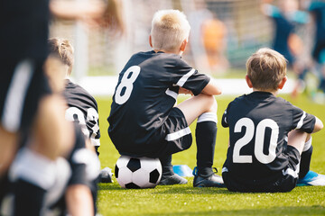 Fototapeta premium Kids in the Sports Team Sitting on Pitch Sideline. Young Football Players. Young Soccer Team Sitting on Bench. Soccer Match For Children. Young Boys Playing Tournament Soccer Match. Youth Soccer Club