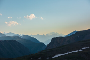 Deep gorge between layered silhouettes of sharp rocky ridge spurs under huge snow-capped mountain...
