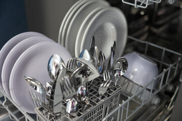 View of the dishwasher with cleaned dishes, plates, bowl, and cutlery. Electric household...