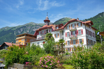 Charming architecture in Brienz, Switzerland, surrounded by lush gardens with flowers and scenic mountains in the background.