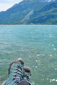Relaxing by the turquoise waters of Lake Brienz in Switzerland, with hiking boots resting on the edge, surrounded by stunning mountains.