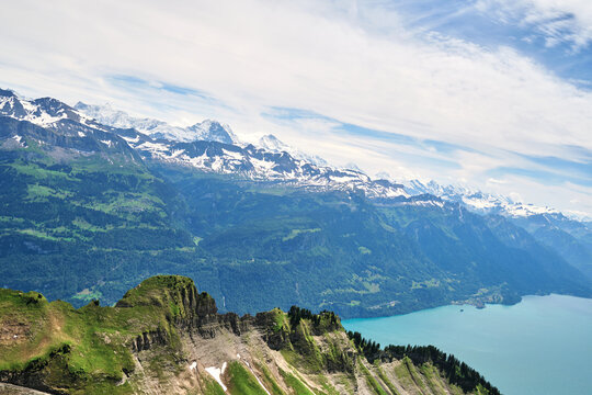 A breathtaking panorama of the Swiss Alps near Brienz, showcasing lush green slopes, rugged cliffs, and a serene turquoise lake under a bright sky.