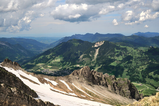Scenic view of the Swiss Alps near Brienz, featuring rugged mountain peaks, lush valleys, and patches of snow under a cloudy sky.